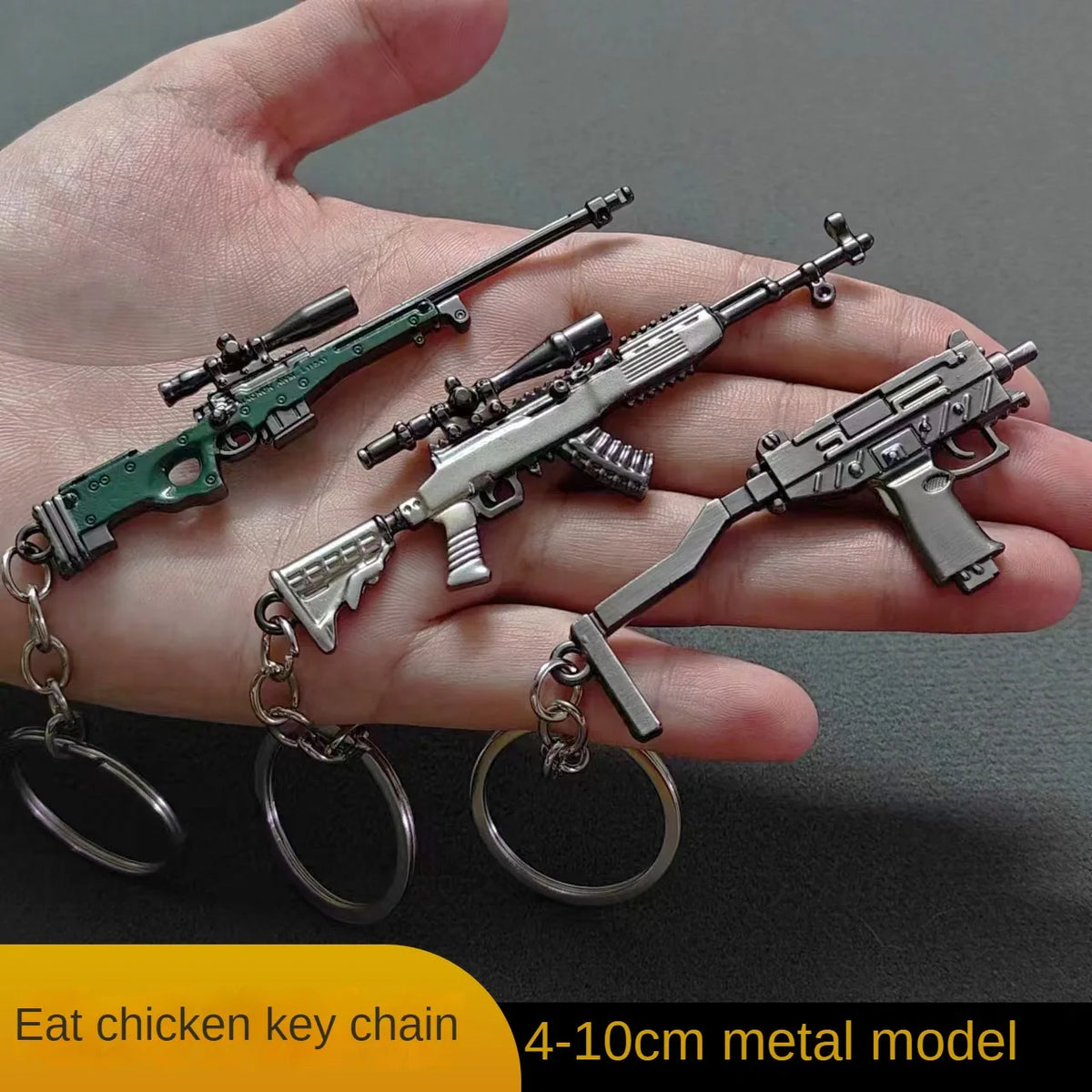 A hand holds an alloy gun model keychain featuring a realistic miniature firearm and chain.