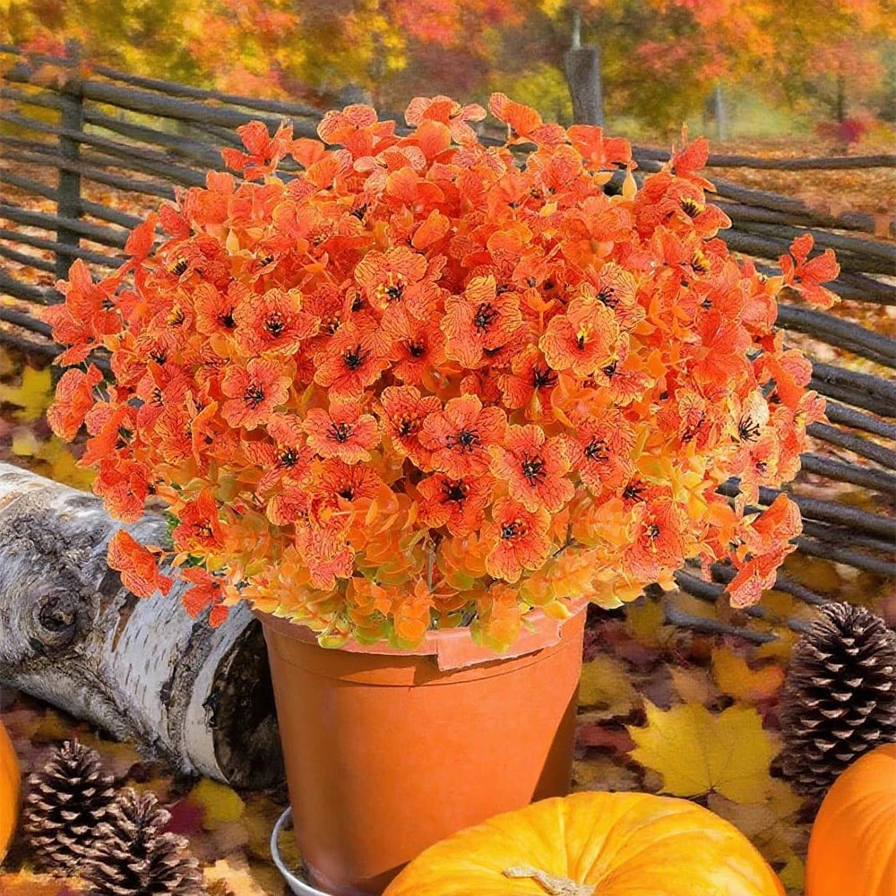 A vibrant bouquet of orange and red artificial fall eucalyptus and flower stems in an orange pot set against a natural outdoo