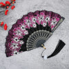 A black folding fan decorated with vibrant pink and white floral patterns on a gray background.