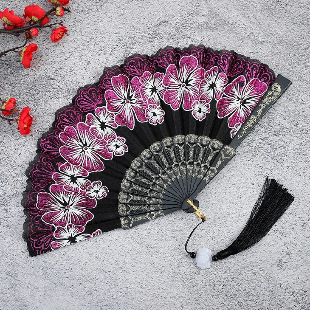 A black folding fan decorated with vibrant pink and white floral patterns on a gray background.