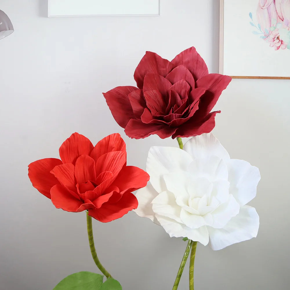 A display of three large foam rose flowers in shades of deep red, bright orange-red, and white against a light gray backgroun