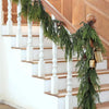 A long garland of artificial Norfolk pine greenery draped along a wooden staircase railing.