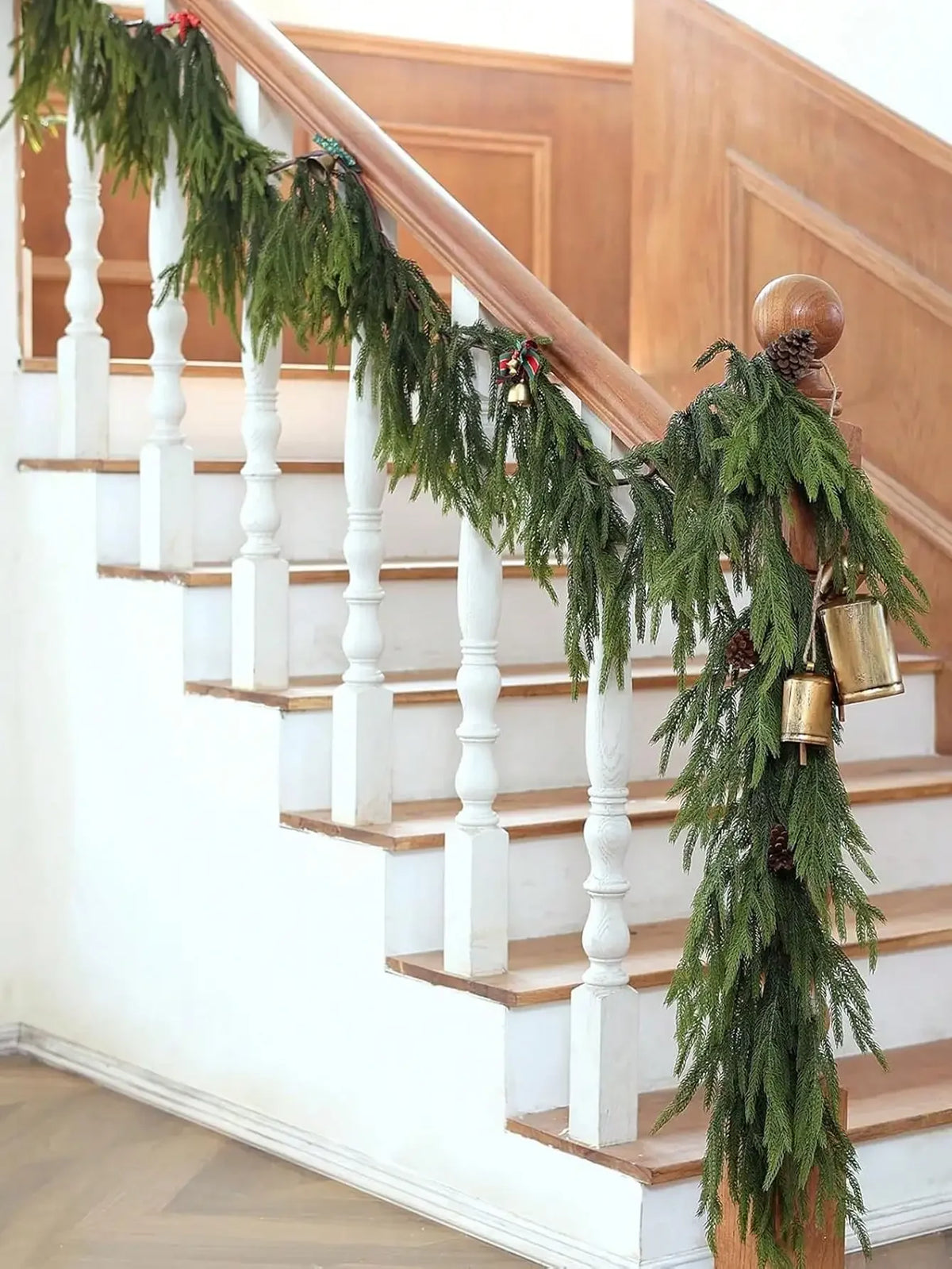 A long garland of artificial Norfolk pine greenery draped along a wooden staircase railing.