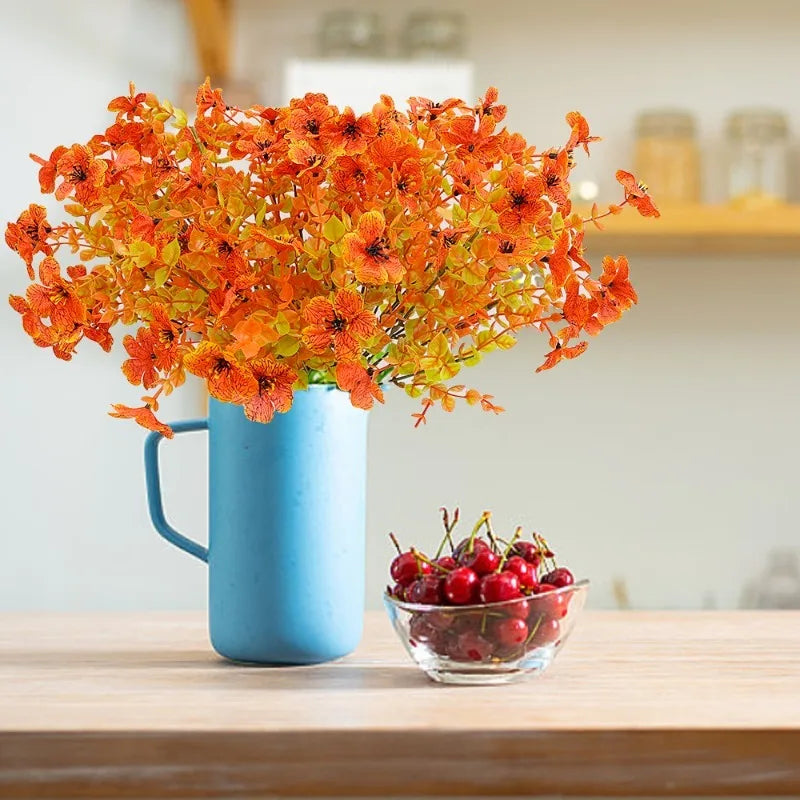 A vibrant orange artificial autumn bouquet in a blue mug sits on a wooden table.