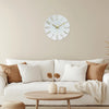 A round white wall clock with gold 3D numerals hangs on a beige wall above a light-colored sofa.