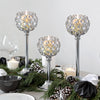 Three elegant metal glass candle holders with flickering candles surrounded by pine greenery and pinecones
