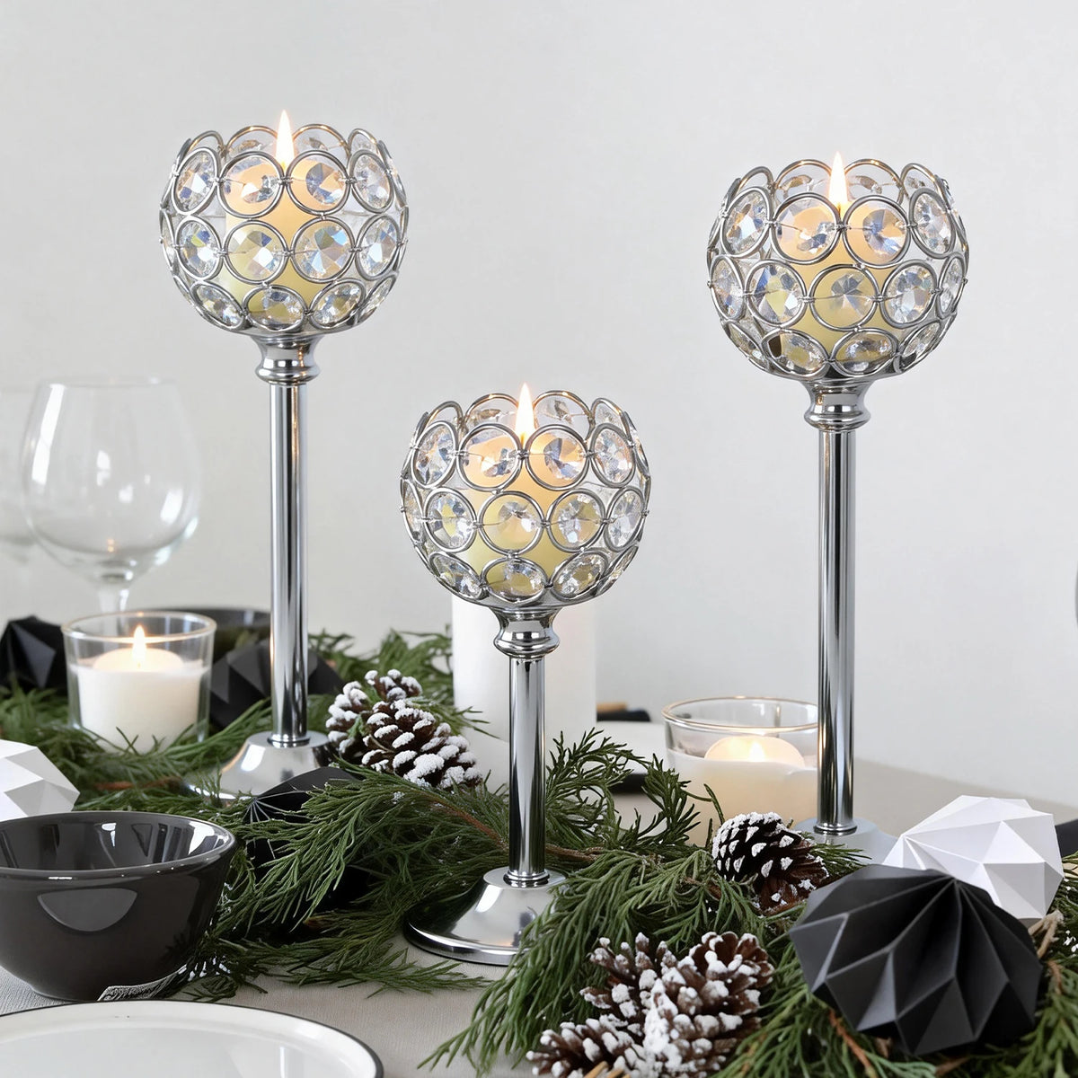 Three elegant metal glass candle holders with flickering candles surrounded by pine greenery and pinecones