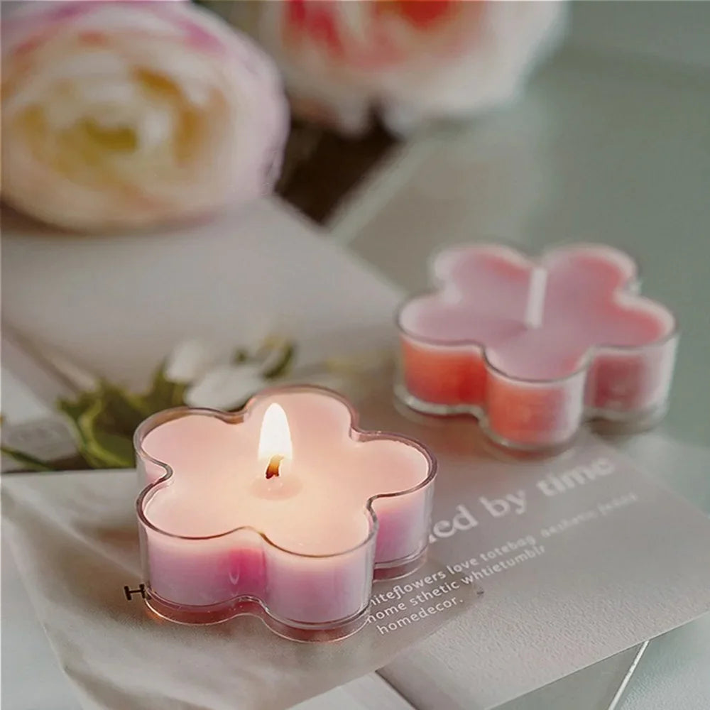 A pink flower-shaped tea light candle in a glass holder resting on white paper.