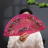 A person holds a pink hand-painted decorative folding fan with floral designs against a dark background.