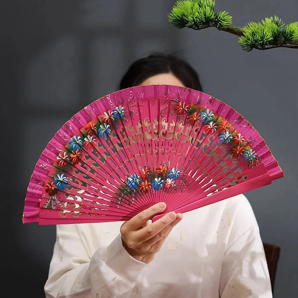 A person holds a pink hand-painted decorative folding fan with floral designs against a dark background.