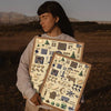 A person holds a framed printable wall art poster featuring various nature and craft-themed illustrations.