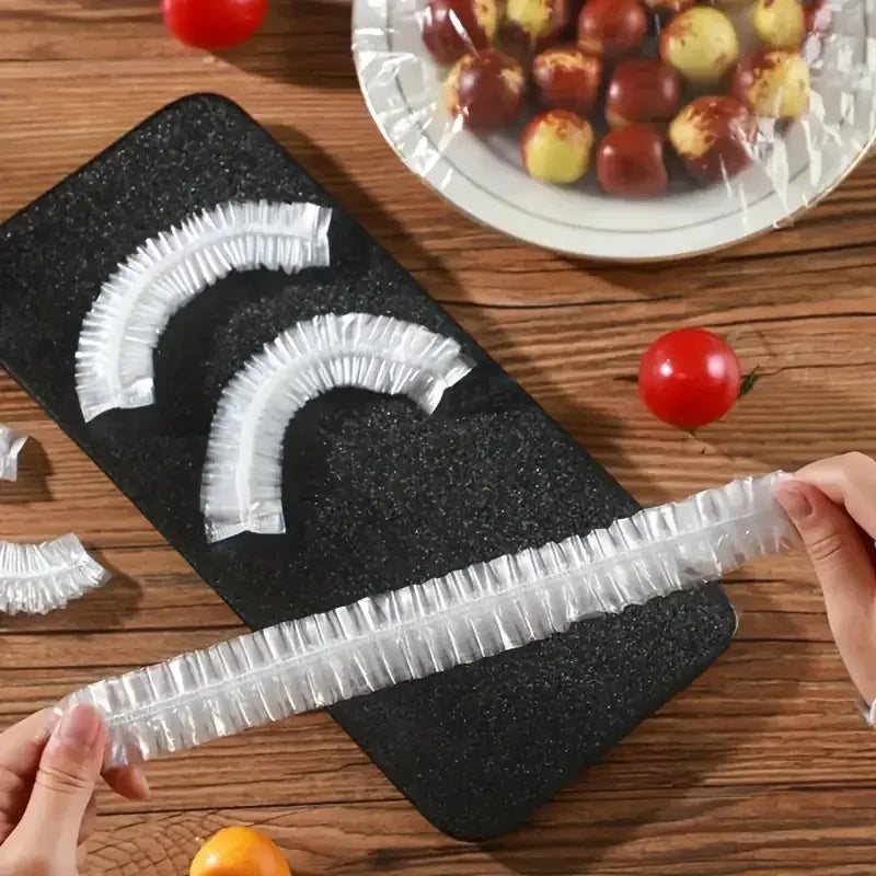 A hand holds a clear reusable food storage bag with decorative bows on a black cutting board next to fresh tomatoes.