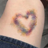 A temporary tattoo resembling a heart bruise in various shades of purple, pink, and yellow on skin.