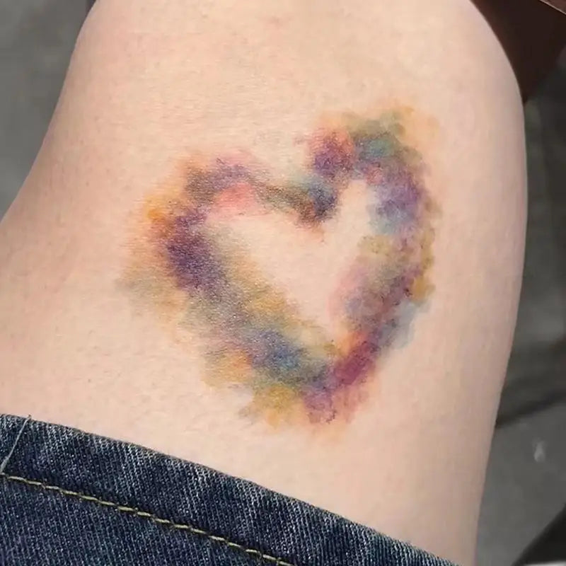 A temporary tattoo resembling a heart bruise in various shades of purple, pink, and yellow on skin.