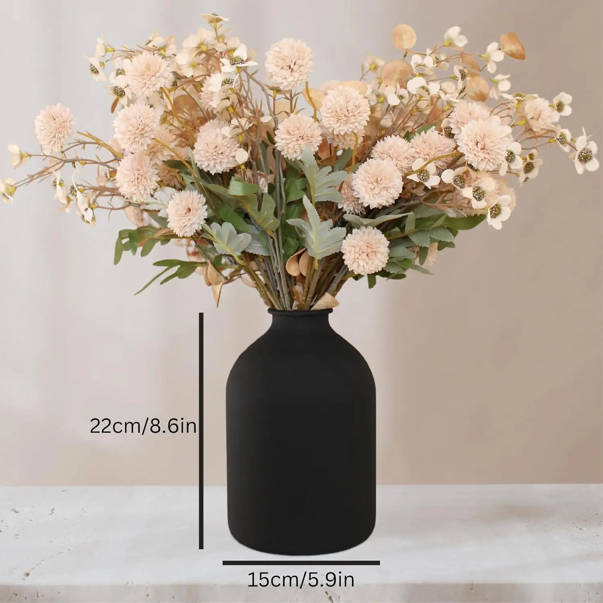 A large matte black decorative vase filled with dried light pink and beige floral arrangements.