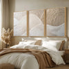 A set of three beige textured abstract canvas wall art prints featuring minimalist mountain lines above a bed.