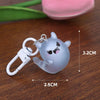 A small, light gray ghost charm with black eyes is attached to a white keyring, shown on a wooden surface.