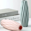 A light mint green decorative plastic vase with vertical ribbed texture next to a pink elongated vase.