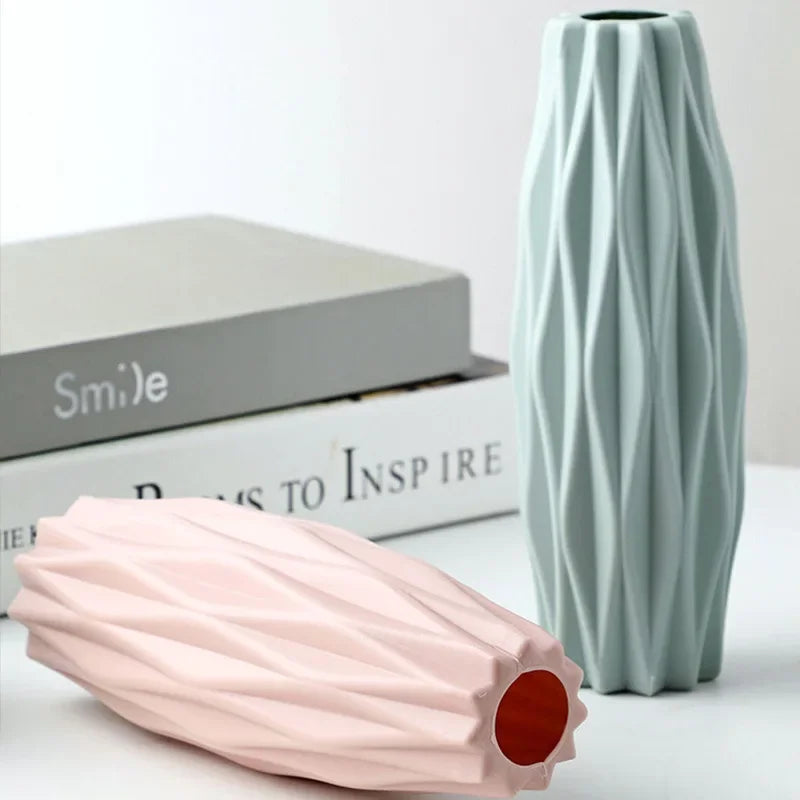 A light mint green decorative plastic vase with vertical ribbed texture next to a pink elongated vase.