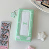 A green photo booth album with a clear window and decorative elements rests on a white surface.
