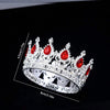 Silver crystal rhinestone crown ring with red gemstones shown against a black background.