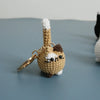 A handcrafted crochet cat keychain pendant in beige and white yarn resting on a gray surface.