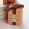 A brown kraft paper gift box tied with a dark brown ribbon and featuring a circular handmade with love stamp.