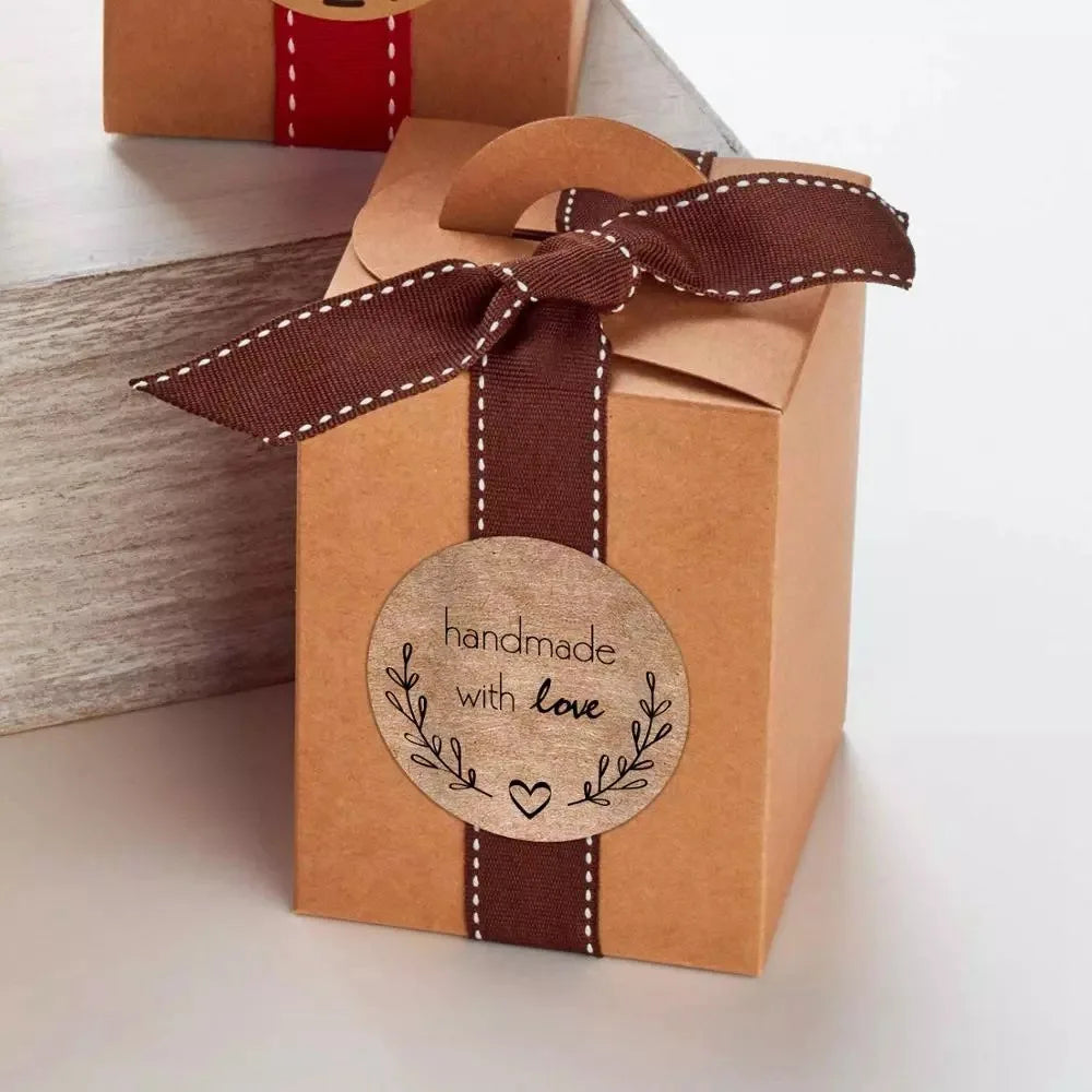 A brown kraft paper gift box tied with a dark brown ribbon and featuring a circular handmade with love stamp.