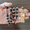 A gold and black rosary necklace featuring a figure of Santa Muerte.