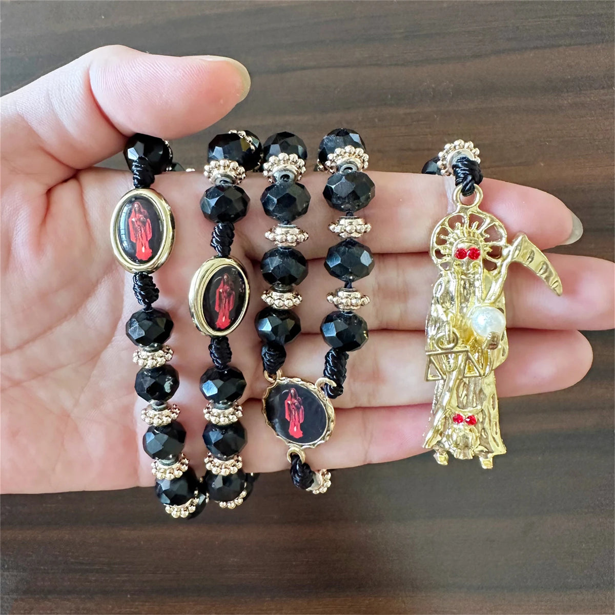 A gold and black rosary necklace featuring a figure of Santa Muerte.
