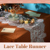 A close-up of a brown linen tablecloth decorated with a white lace table runner, floral accents, and small cards.
