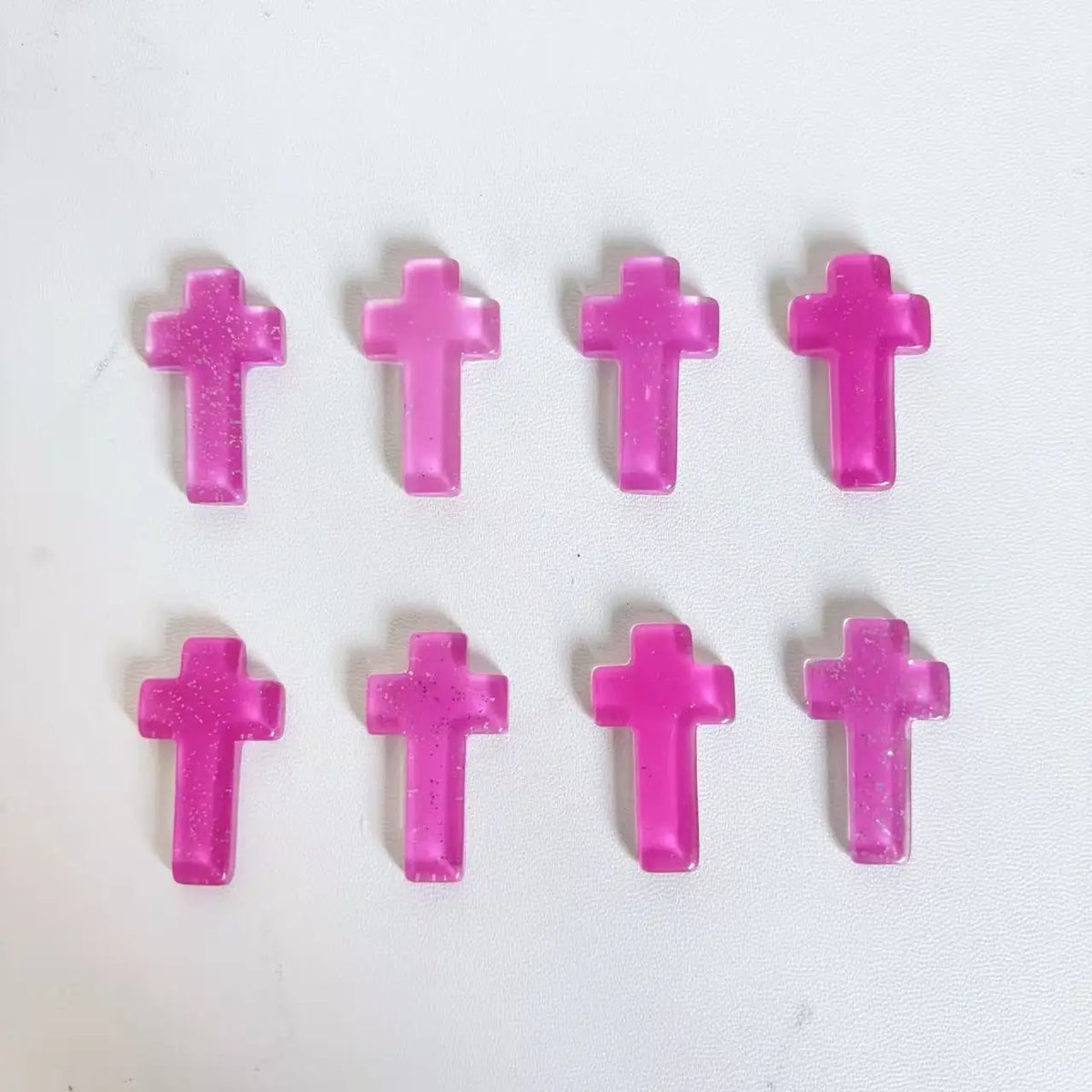 Sechs rosa glitzernde Kristallkreuze in einer Reihe angeordnet.