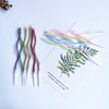 A collection of curved metallic birthday cake candles in various pastel colors are displayed on a white background.