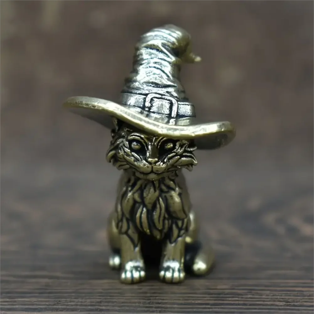Vintage brass cat statue wearing a witch hat, sitting on a wooden surface.