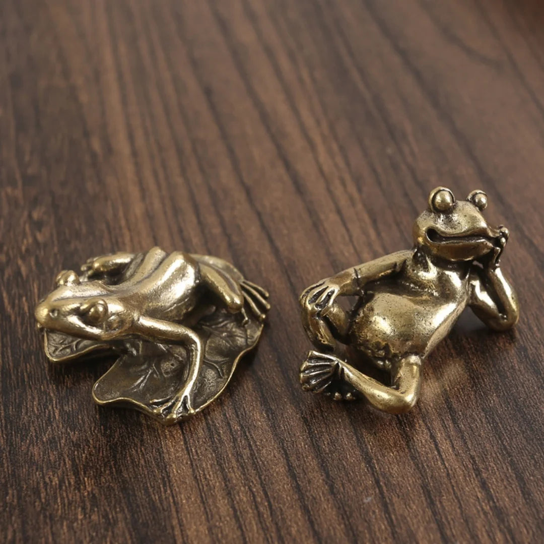Antique brass frog sculpture decor resting on a dark wooden surface.