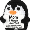 A black and white crochet penguin plush doll with an orange beak and a tag that reads Mom I Flippin Love You