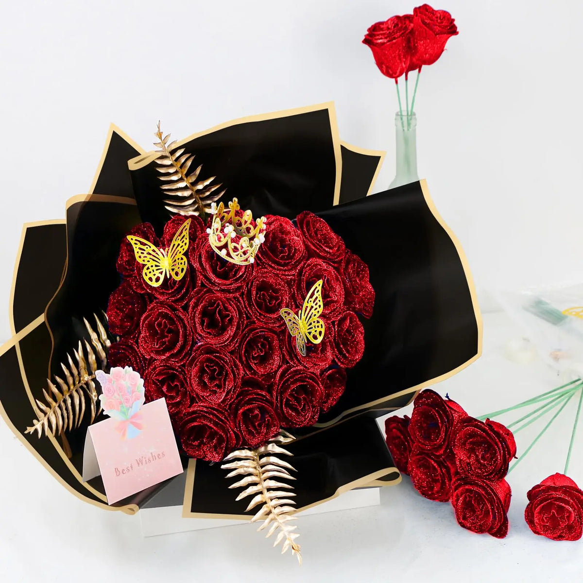 A bouquet of deep red artificial roses with gold glitter accents displayed in a black decorative box.