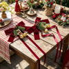 Festive Christmas curtain tie-backs with red bows and pinecones displayed on a wooden table.