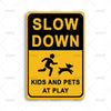 A yellow rectangular sign with black text that reads SLOW DOWN KIDS AND PETS AT PLAY