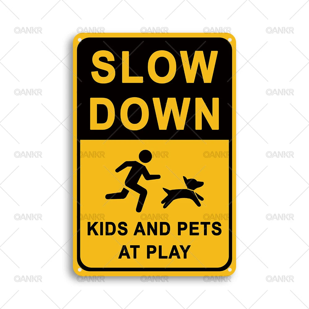 A yellow rectangular sign with black text that reads SLOW DOWN KIDS AND PETS AT PLAY
