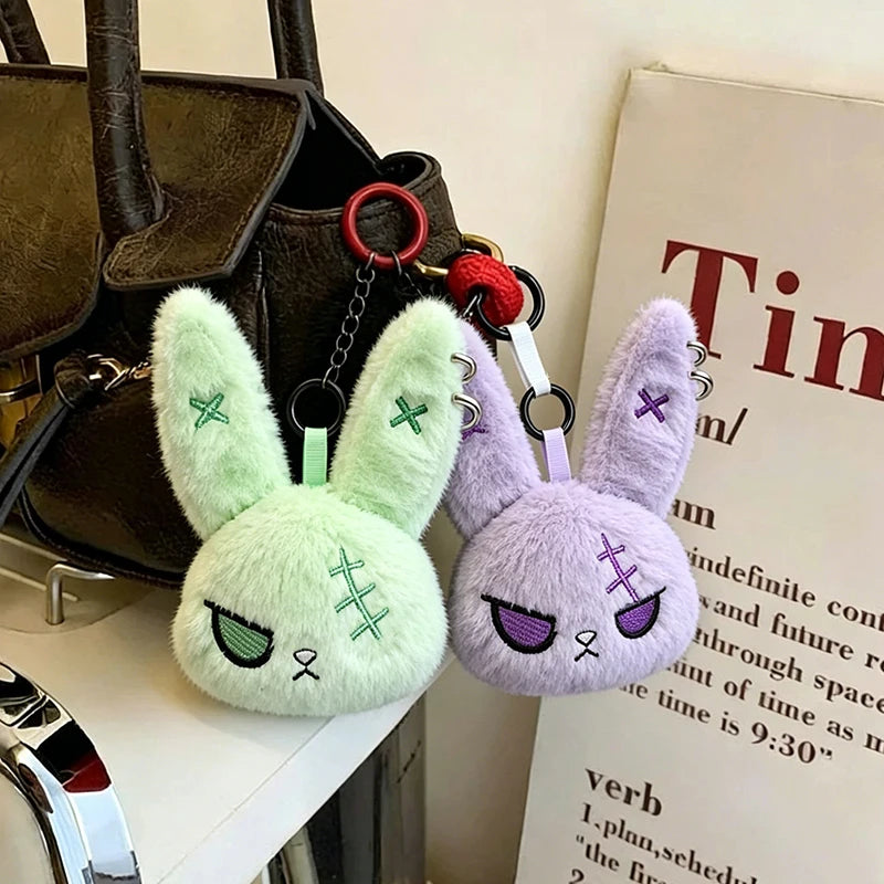 A light green bunny plush keychain with purple accents is displayed next to a dark brown handbag.