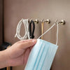 A hand holds a light blue disposable face mask near magnetic hooks on a wall.