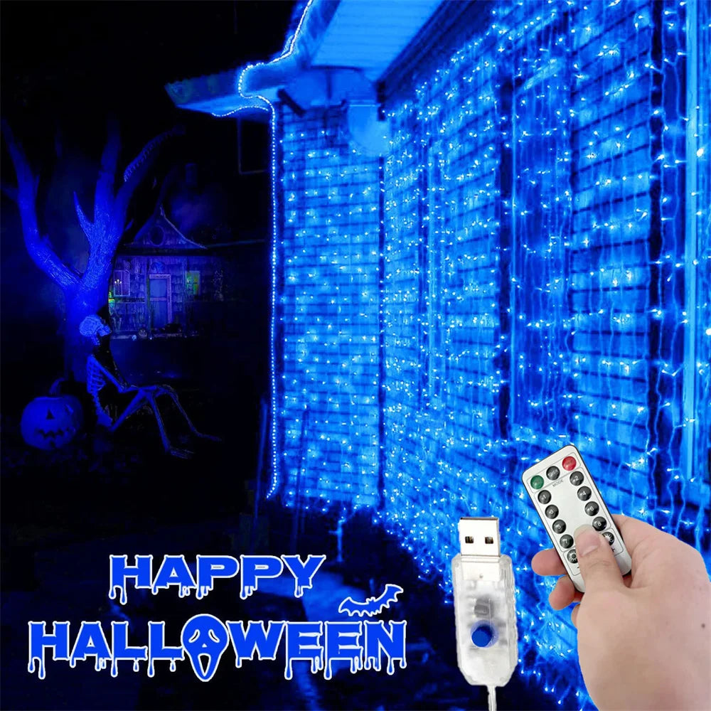 A hand holds a remote control for blue LED curtain fairy lights illuminating a building facade in a Halloween setting.