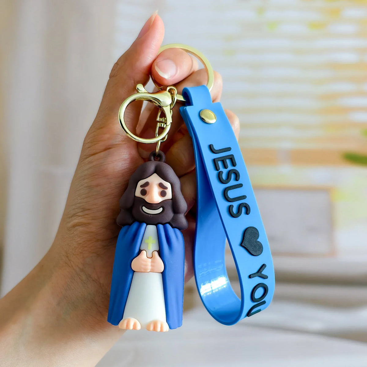 A hand holds a silicone keychain featuring a Jesus figure and a blue strap engraved with the words Jesus You