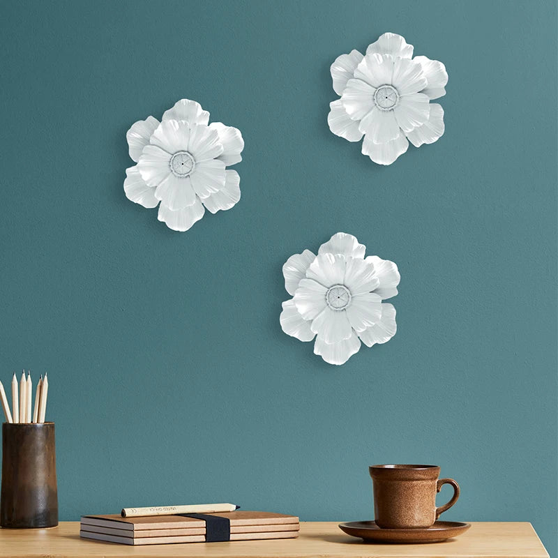 Three white flower-shaped resin wall art pieces displayed on a teal wall above a wooden table.