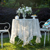 Elegant white floral lace tablecloth displayed on a table outdoors with a white vase of flowers.