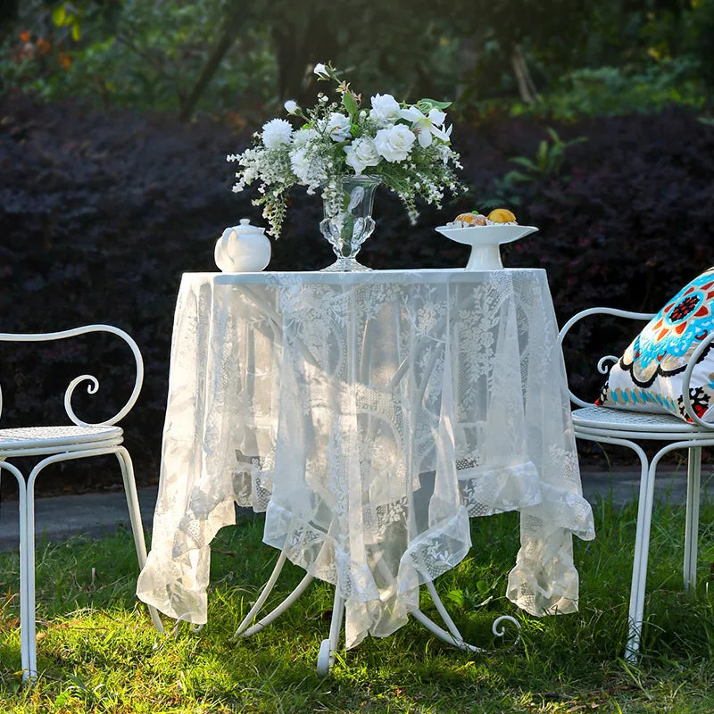 Elegant white floral lace tablecloth displayed on a table outdoors with a white vase of flowers.