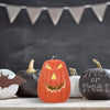 An orange carved pumpkin decoration with a menacing face displayed on a white surface.