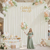 A white fabric backdrop curtain decorated with balloons and greenery for a celebration.