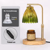 A brass adjustable candle warmer lamp with a green glass shade and a wooden base, showing the heating bulb and timer feature.